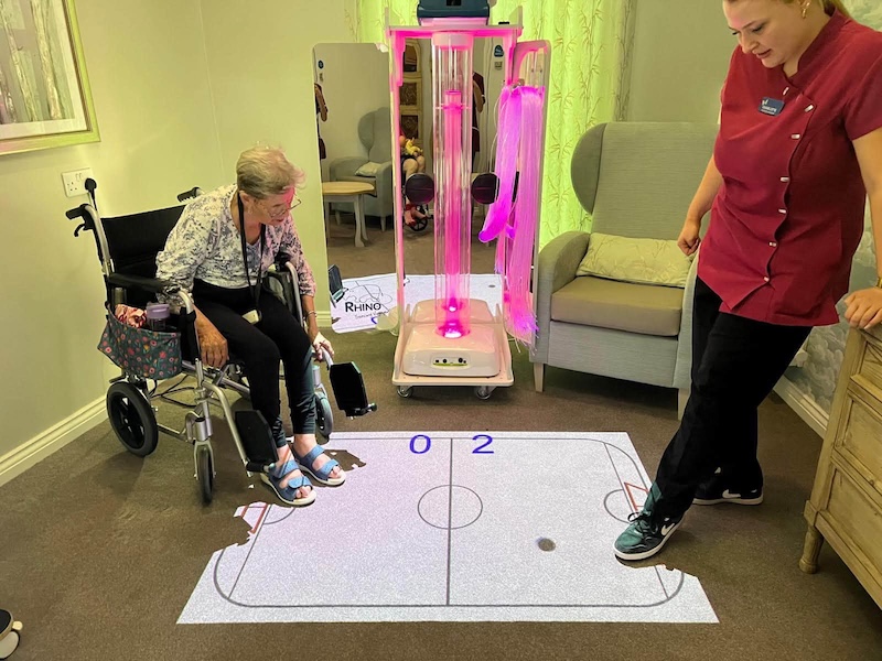 one of our residents and activities coordinators playing air hockey on a table projected onto the ground of our lounge