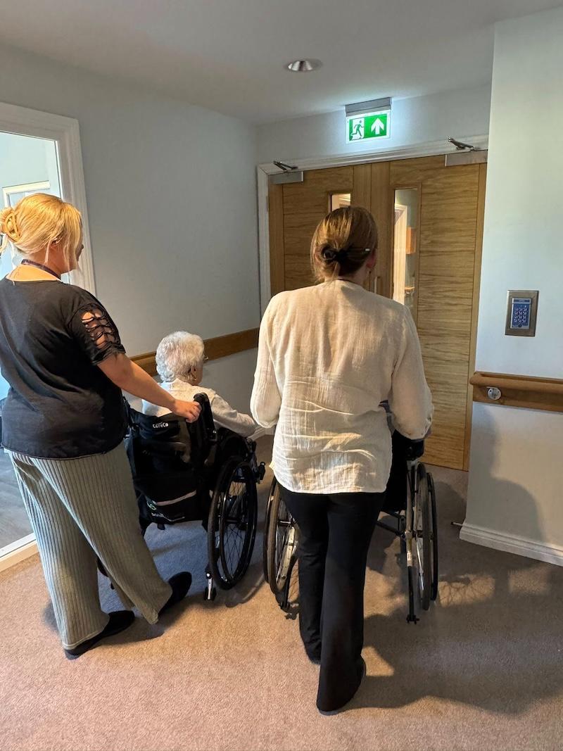 two residents in wheelchairs opening the doors of a brand new floor
