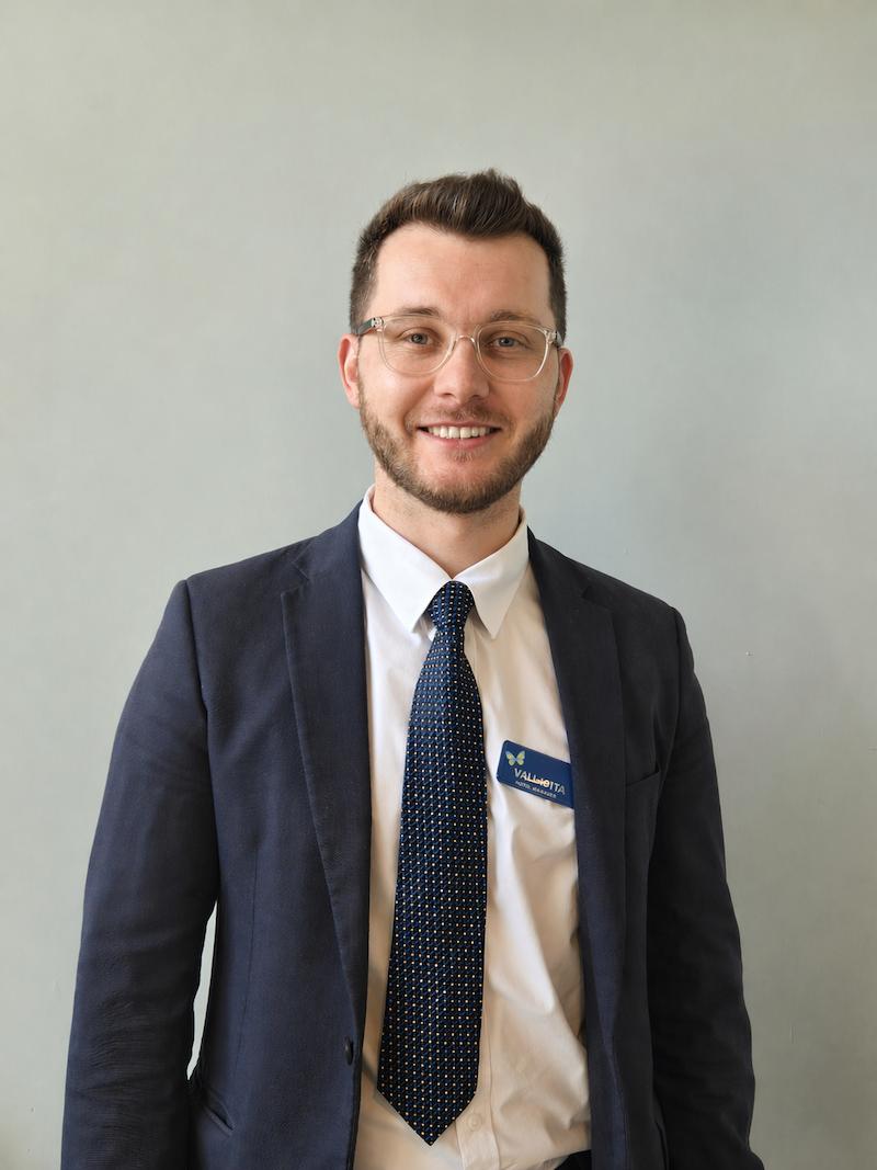 home manager stood smiling wearing a suit having his photo taken for the team page