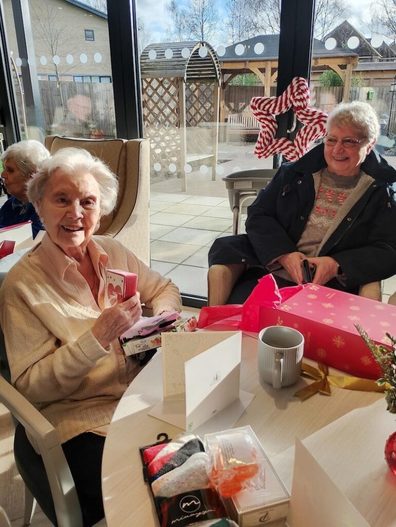 two elderly ladies sat around a table on Christmas opening presents