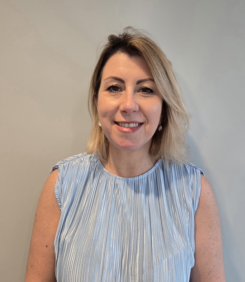 lady with blonde hair wearing a blue top smiling having her photo taken for the team page