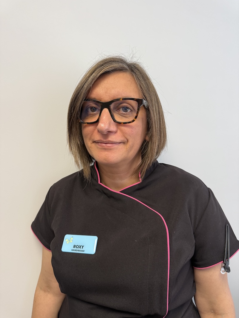 woman with brown hair wearing a hairdressers uniform smiling having her photo taken for the team page