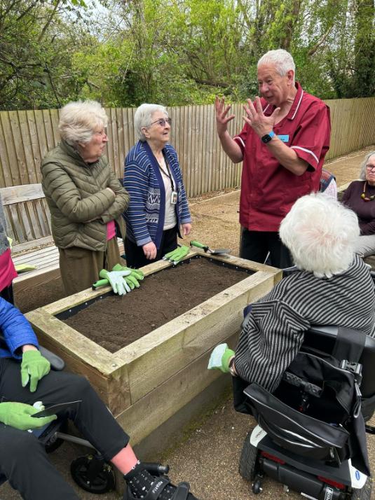 carer standing with residents planting potatoes