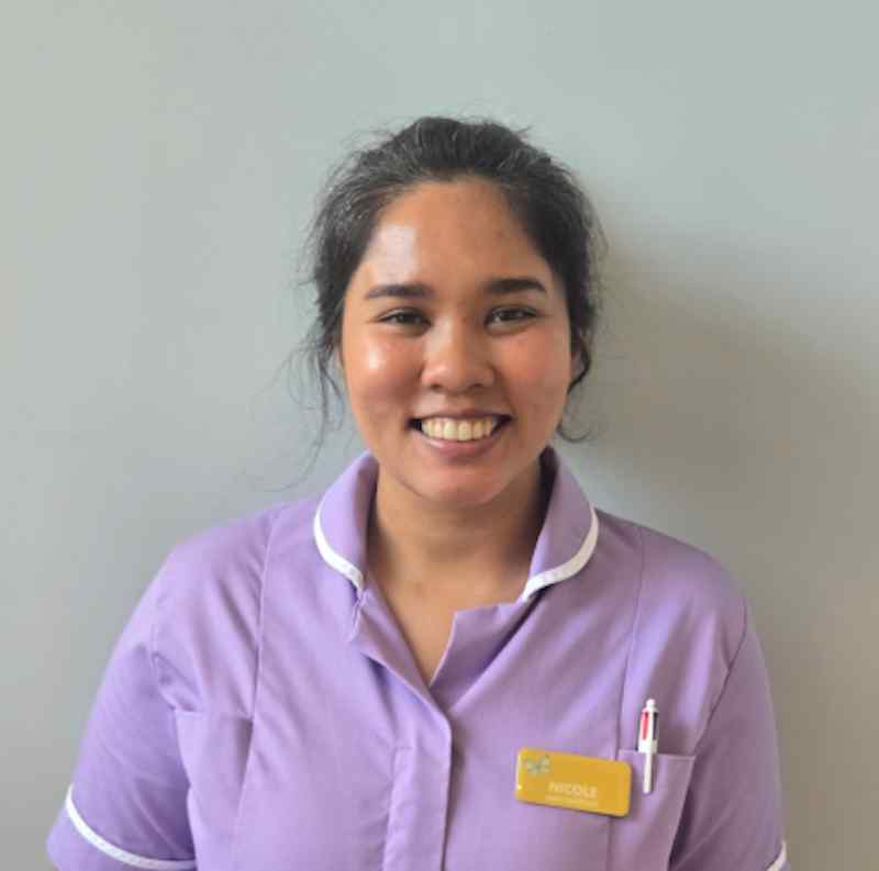 female care assistant stood smiling wearing a lilac nurse uniform