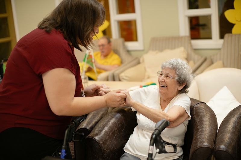 female resident sat down smiling and holding hands with a carer