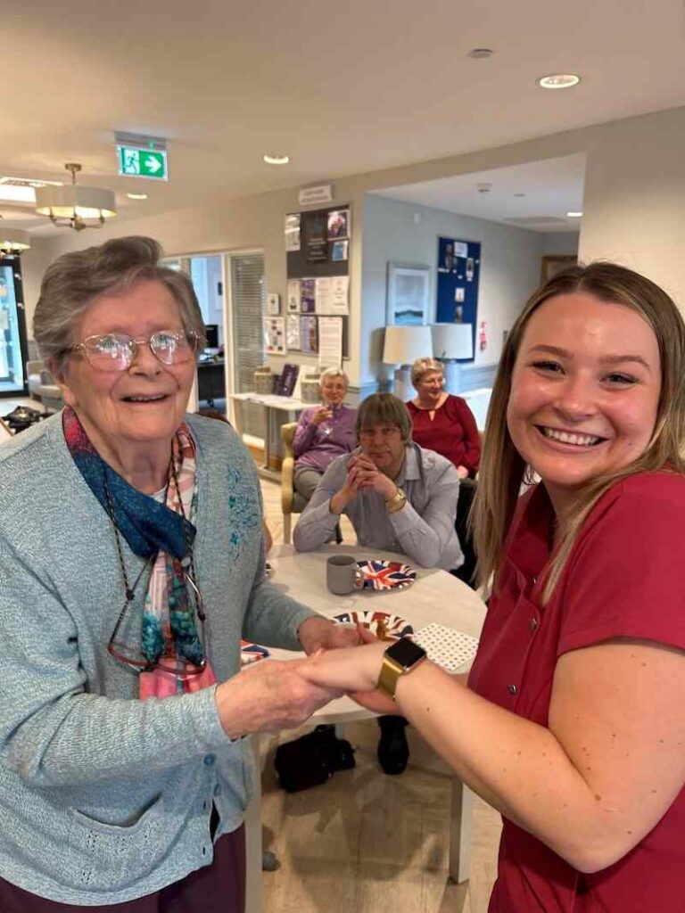 female resident stood smiling and holding hands with an activities coordinator