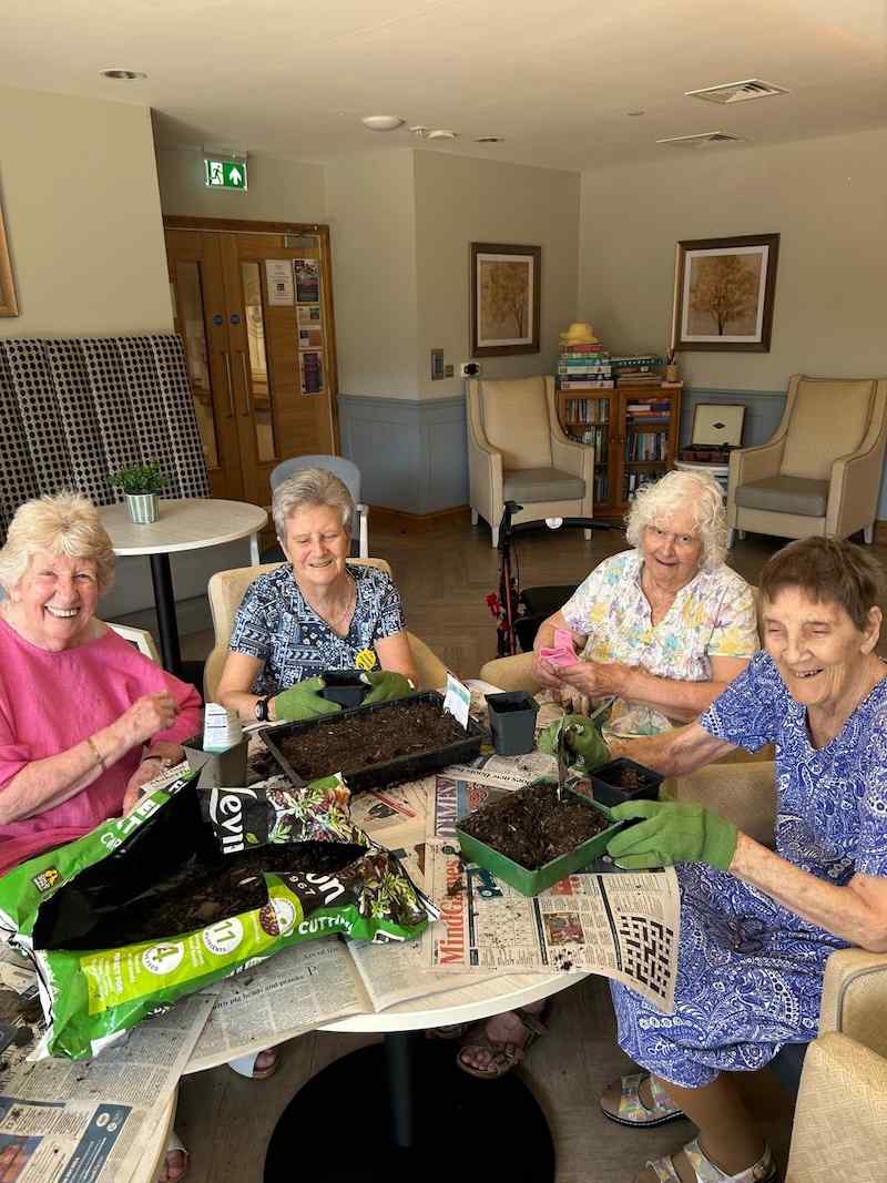 4 female residents sat around a table together doing indoor gardening