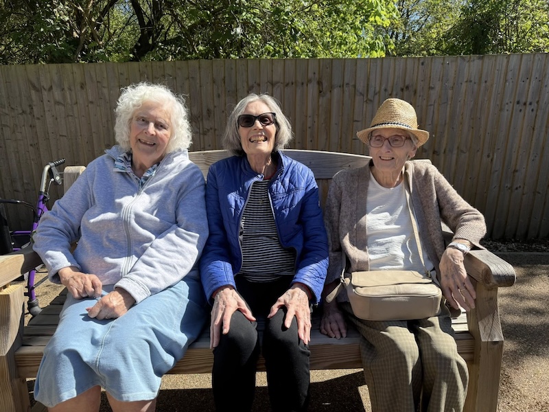 3 female residents sat down on a bench outside smiling