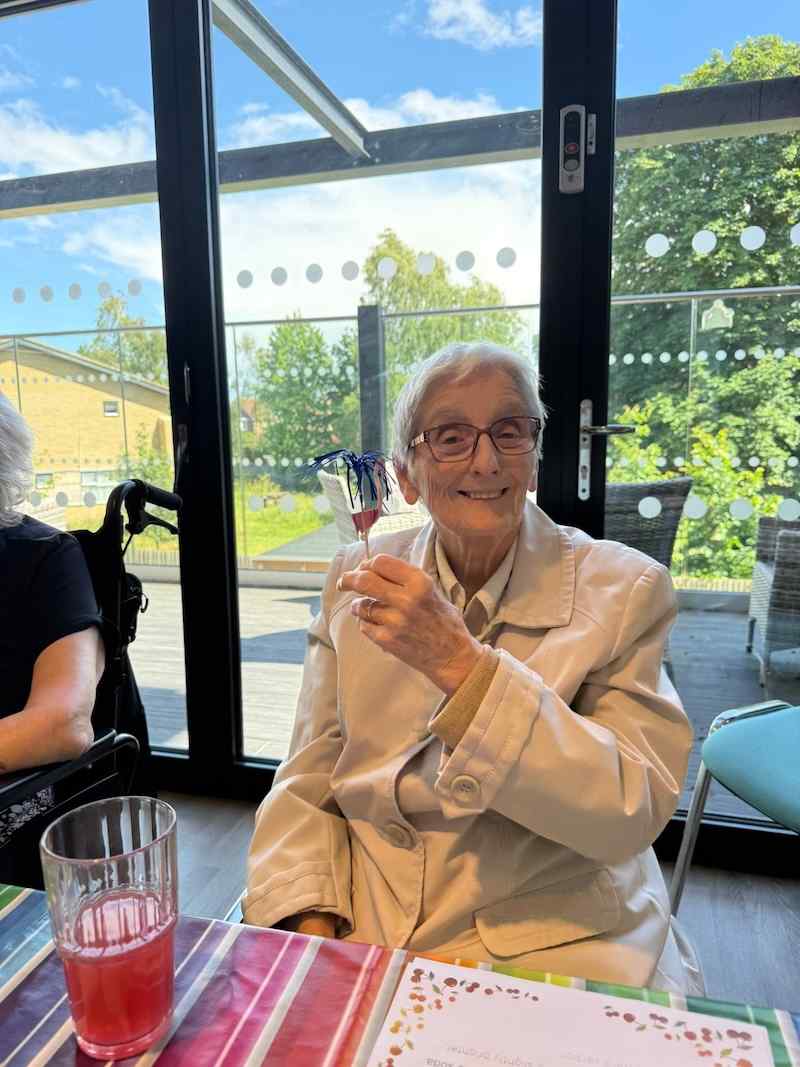 one of our residents wearing a cream jacket holding a drink smiling