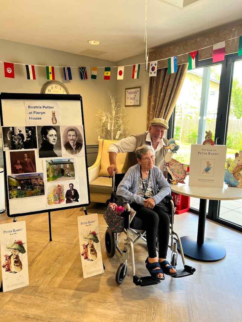 one of our residents in her wheelchair smiling with our activities coordinator and peter rabbit display