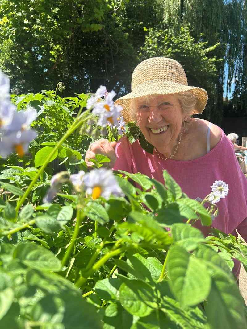 One of our female residents wearing a straw hat stood in the garden by the flowers smiling